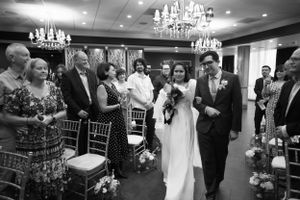 Wedding ceremony guests stand as couple walks down aisle under crystal chandeliers.
