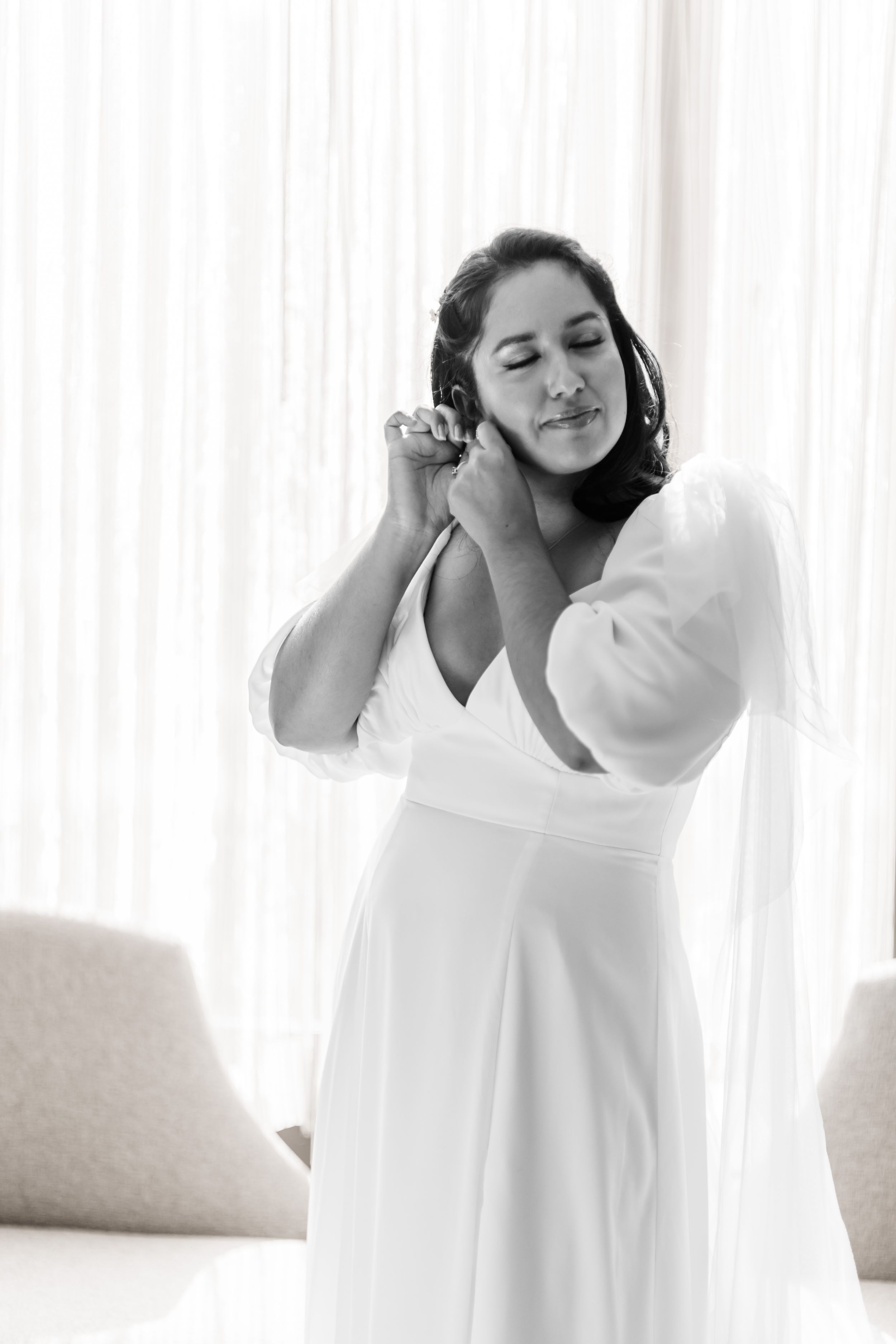 Black and white portrait of person in white dress adjusting jewelry.