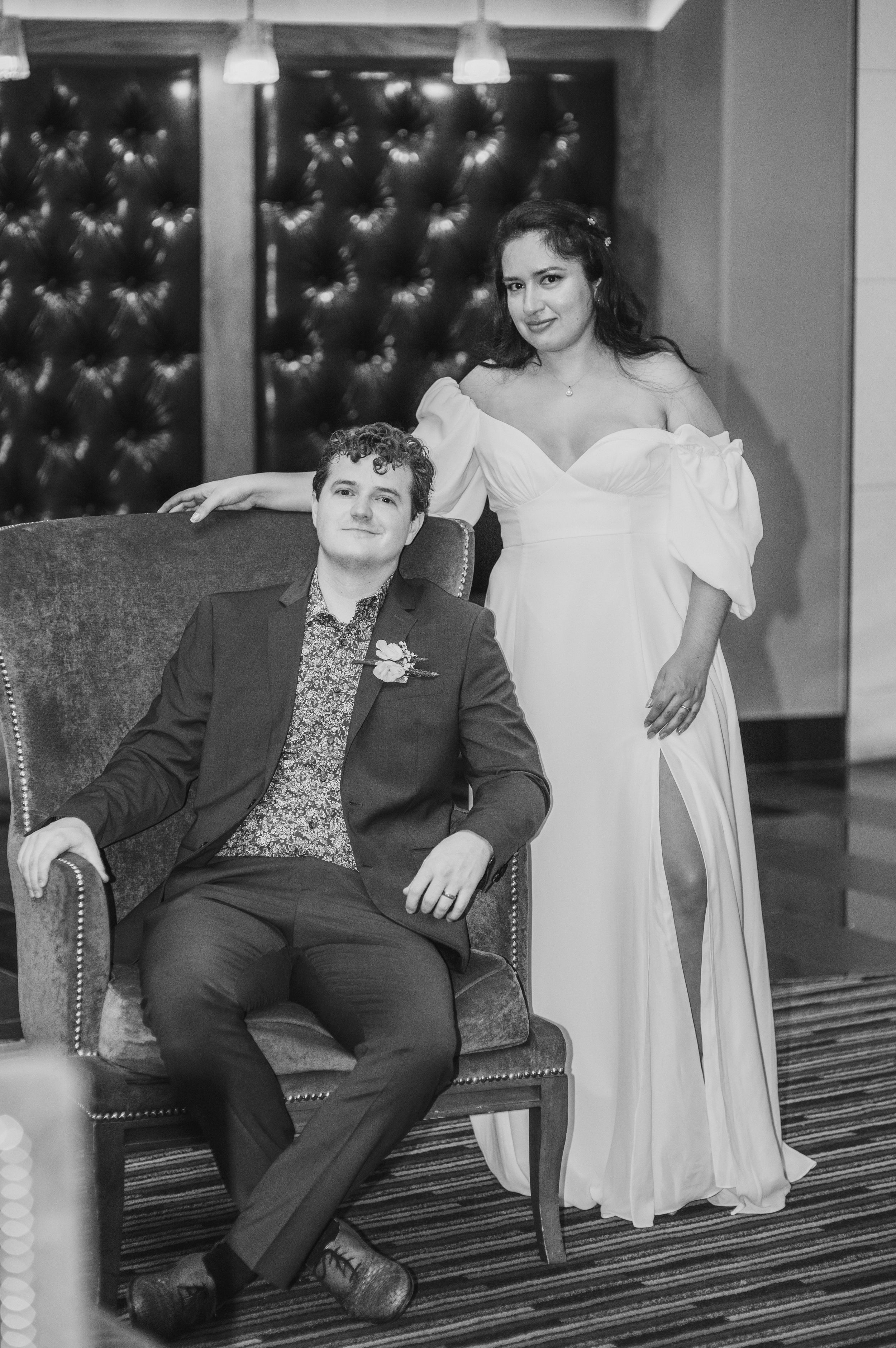 Elegant couple posing in formal wedding attire against a tufted wall.