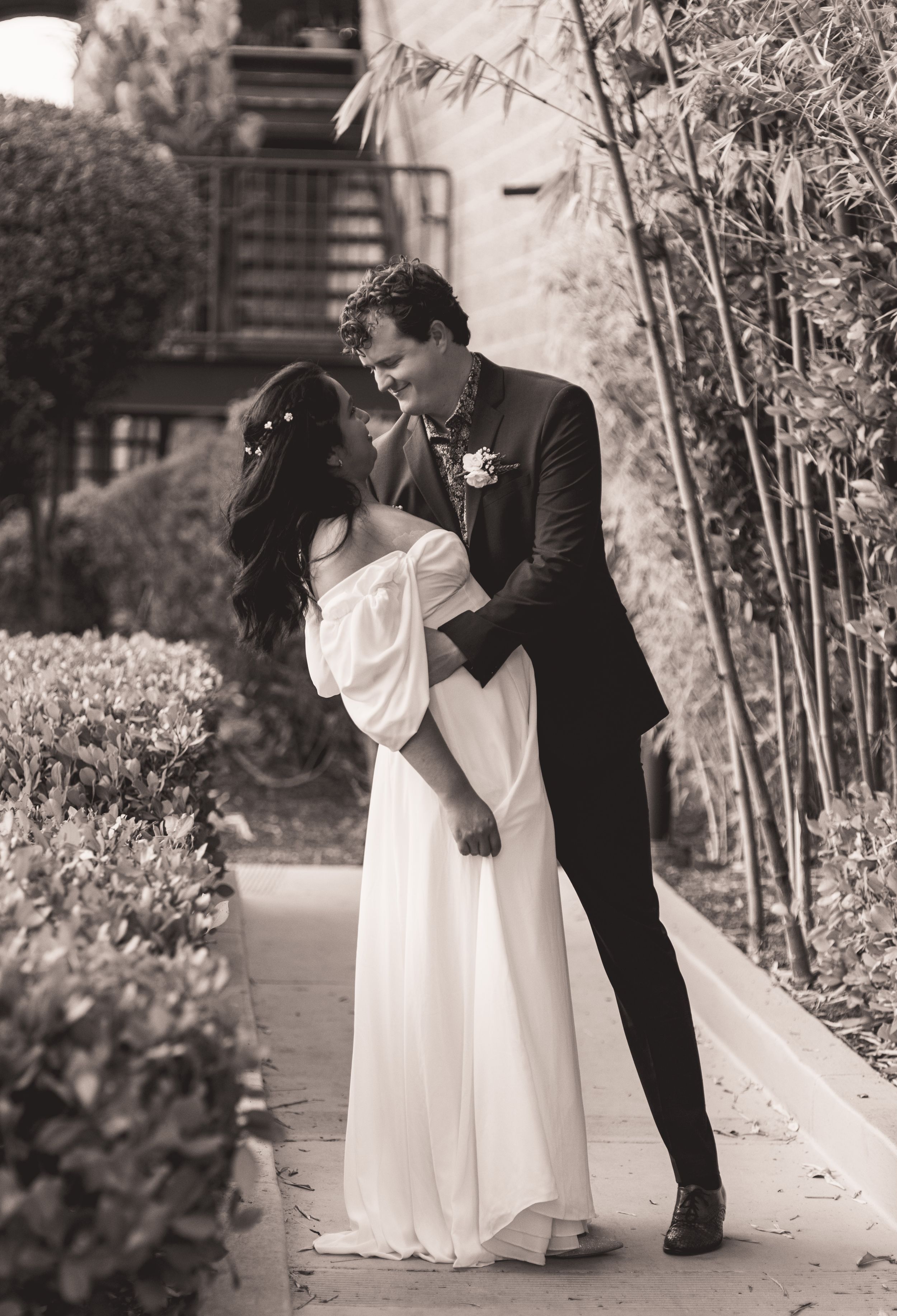 Romantic black and white photo of couple embracing in a garden setting.