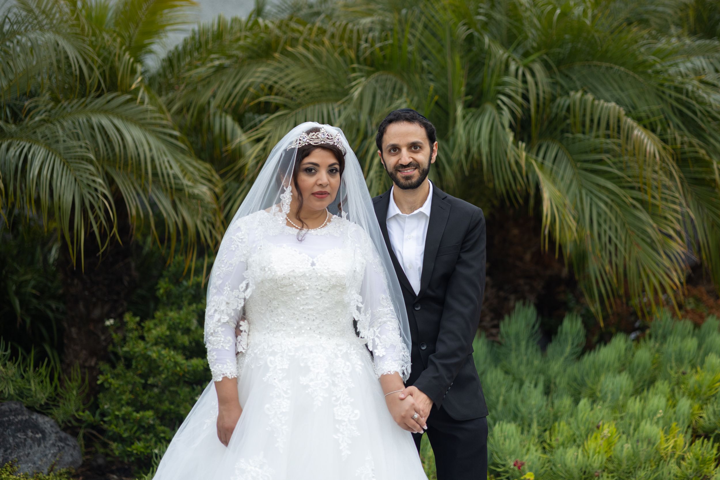 Wedding portrait with palm trees featuring couple in traditional wedding attire.