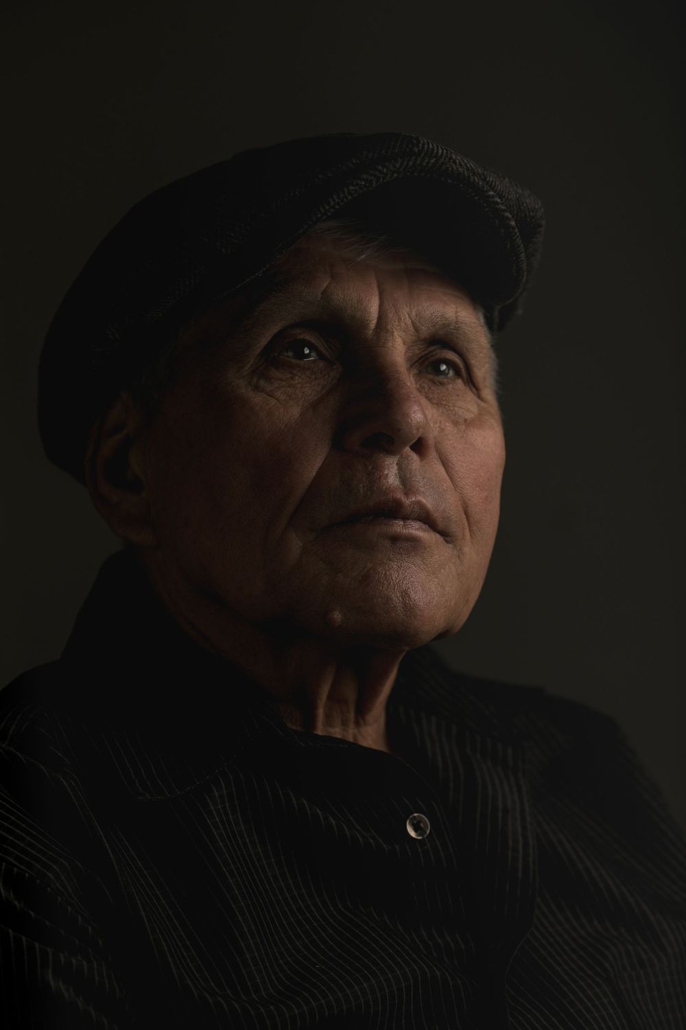 Dramatic low-key portrait in dark lighting with black cap.