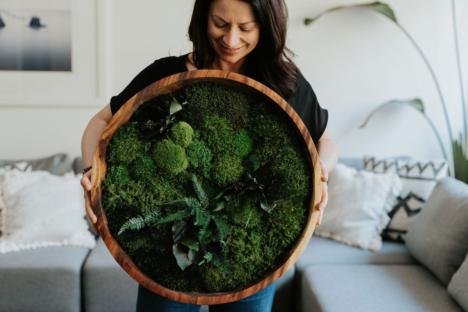 Woman holding round, wood framed moss art.