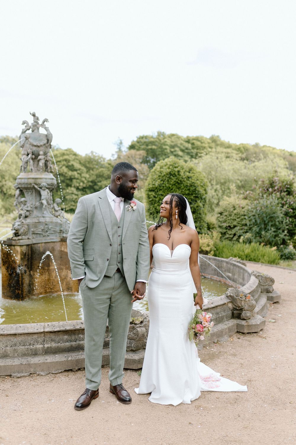 Wedding couple pose together near an ornate stone fountain in a romantic garden setting at Colwick Hall.