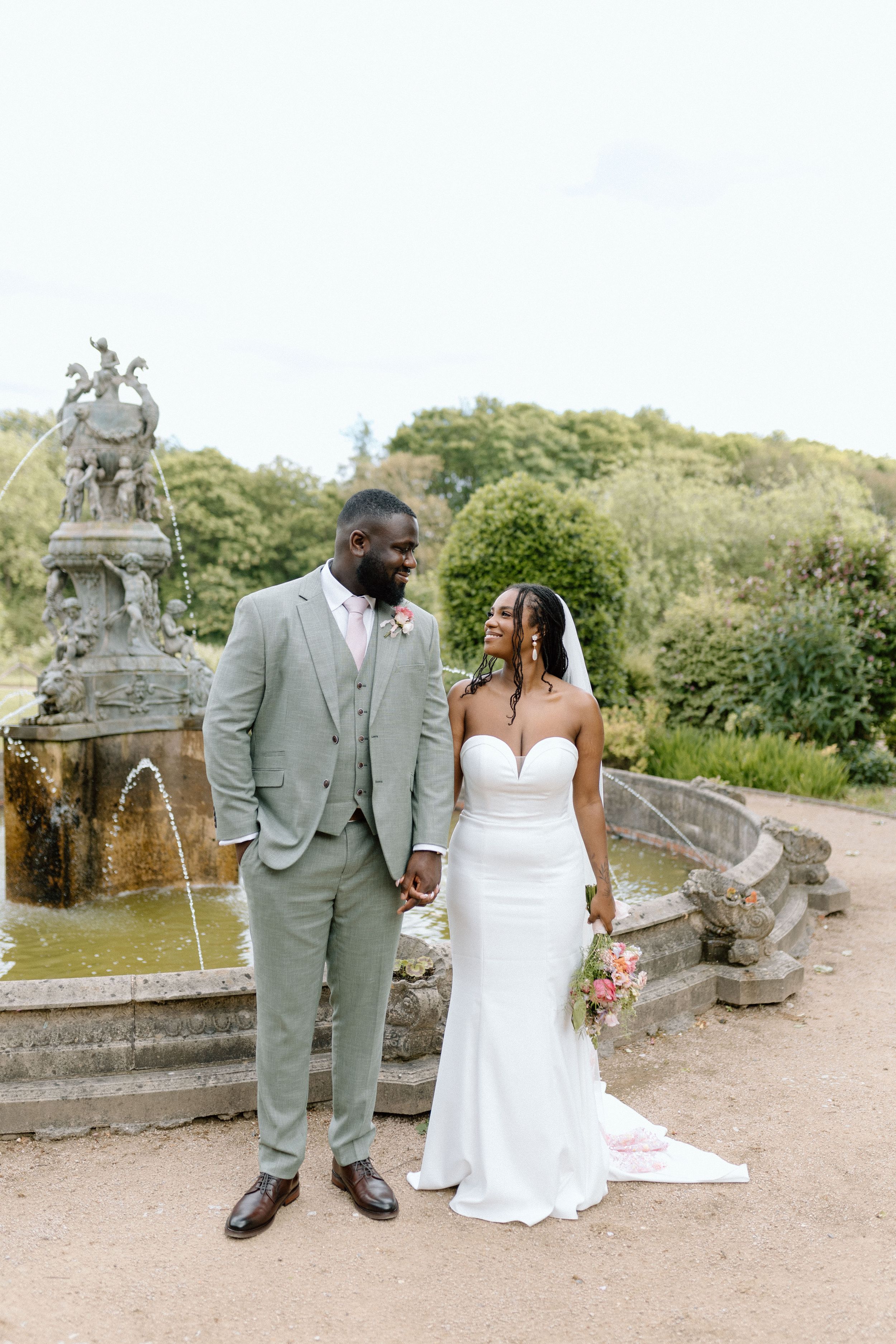 Wedding couple pose together near an ornate stone fountain in a romantic garden setting at Colwick Hall.