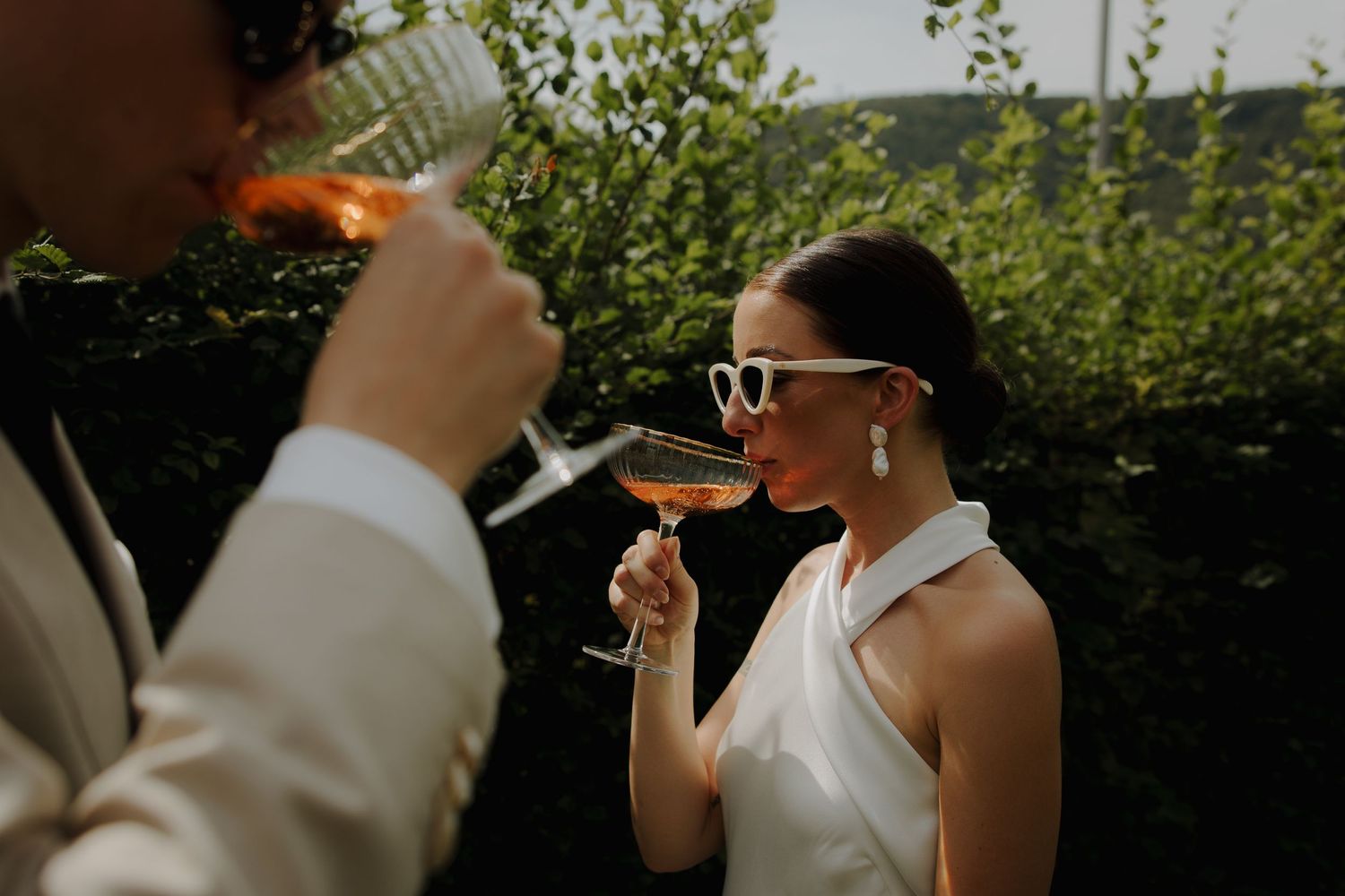 Two people in formal attire sharing drinks and laughing at an outdoor celebration.