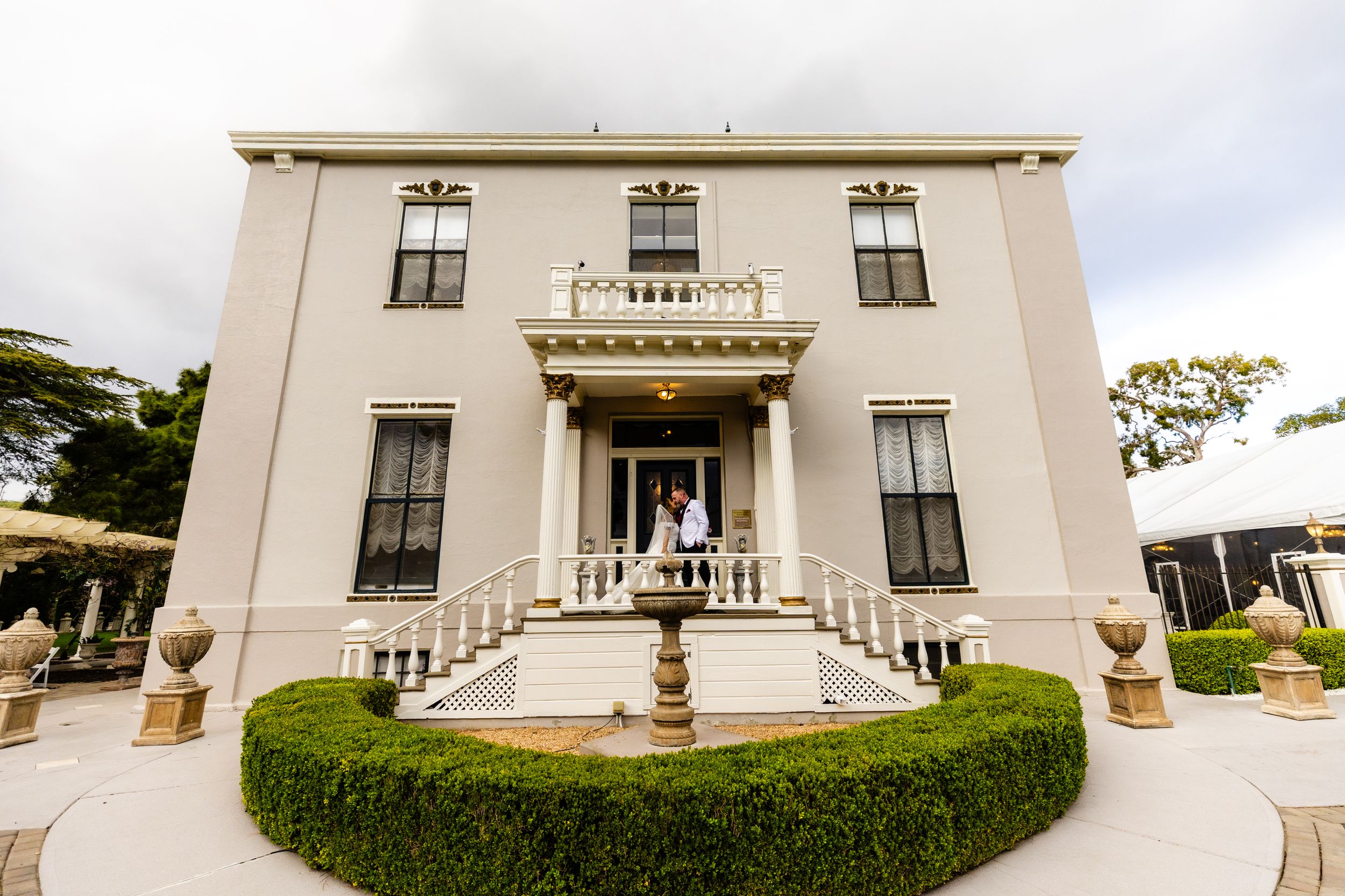 Stately white mansion with ornate architectural details and manicured hedges.