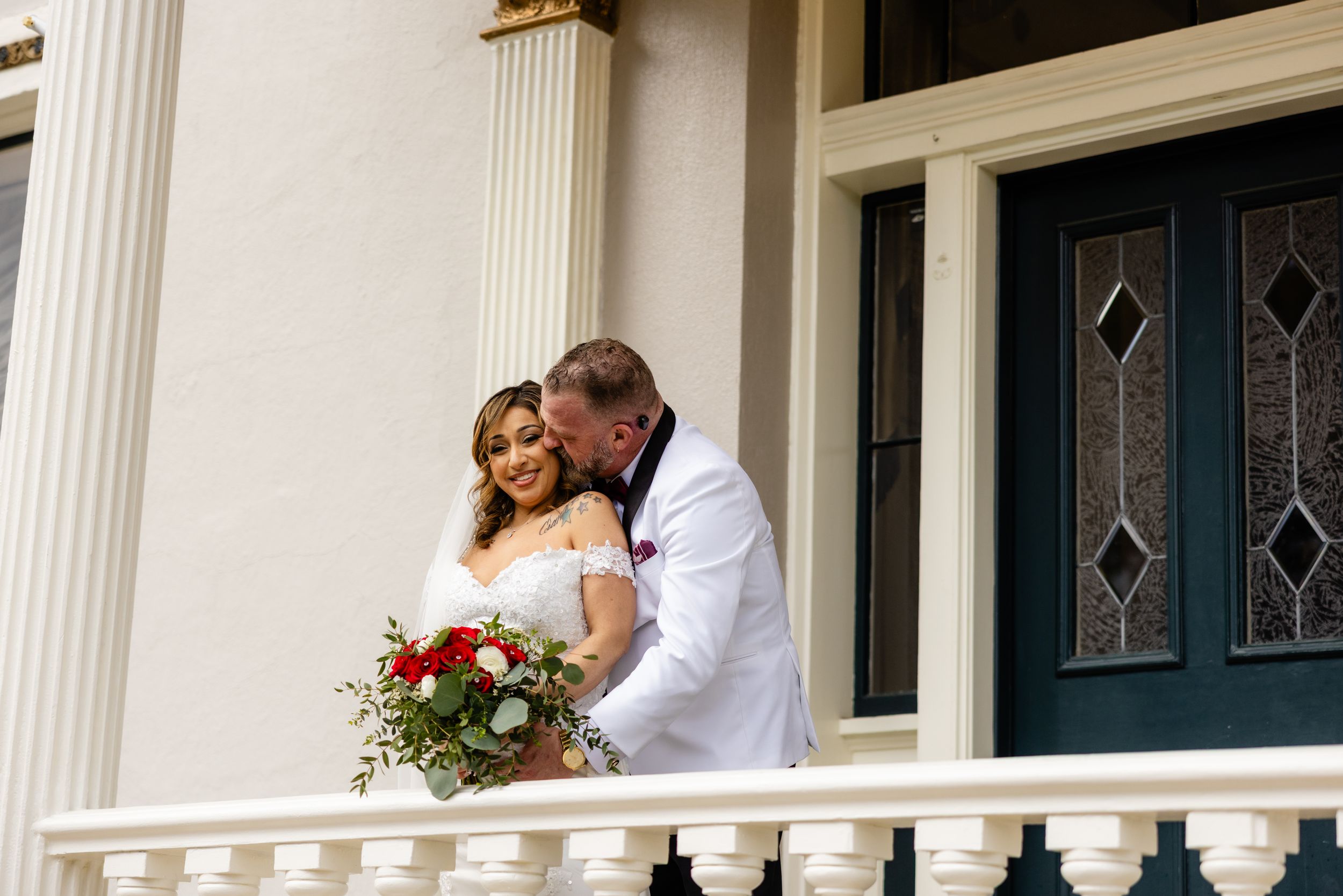 Romantic wedding moment captured on white columned porch of historic building.