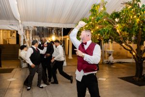 Guests dancing and celebrating at an indoor wedding reception with decorative trees and twinkle lights.