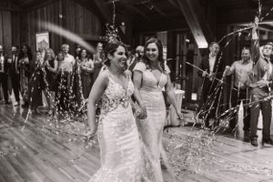 Two people in elegant wedding dresses celebrate on a wooden dance floor surrounded by sparklers.