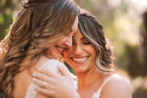 Two people share an intimate embrace and smile in warm sunlit outdoor setting.