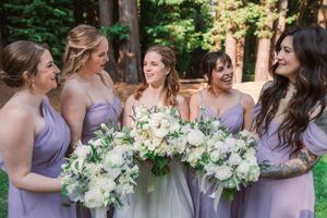 Bridesmaids in purple dresses gather with white bouquets during outdoor wedding.