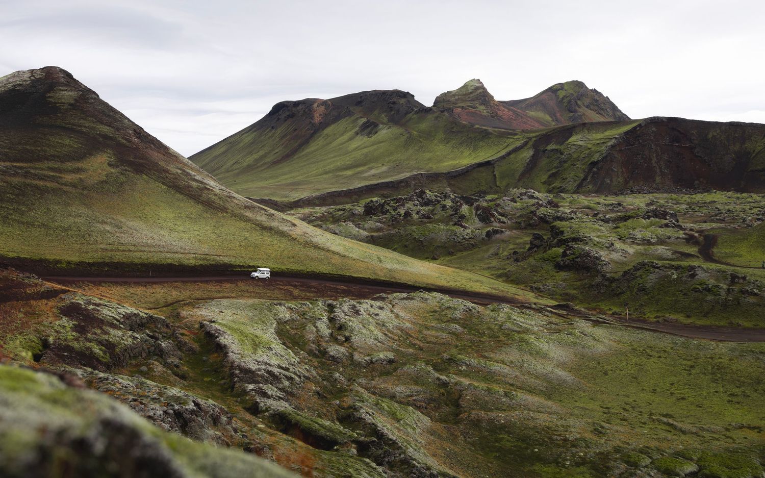 Scenic mountain pass with winding road through green slopes under overcast sky.