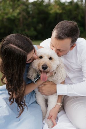 A couple in casual attire cuddles with their fluffy white dog on a light-colored surface in a series of sweet moments.