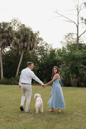 A couple in light blue and white outfits playing with their white dog in a grassy field.
