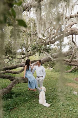 A couple shares a romantic moment under Spanish moss-draped trees in a dreamy outdoor setting.