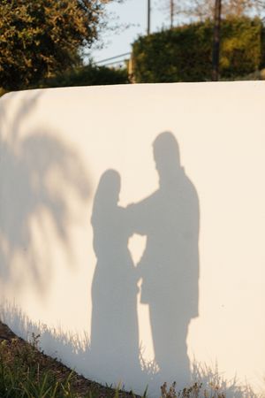 Silhouettes of two figures cast shadows against a white wall during sunset, creating a romantic scene.
