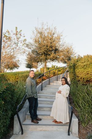 A couple poses on concrete steps with handrails and landscaping during an outdoor photoshoot.