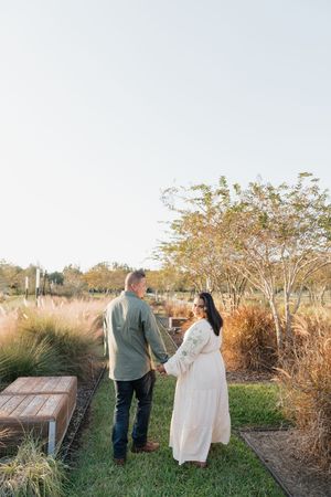 A couple walks together through a garden path surrounded by autumn foliage and ornamental grasses in golden light.