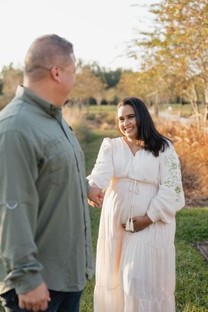 A couple shares a romantic moment in a field during golden hour with autumn trees in the background.