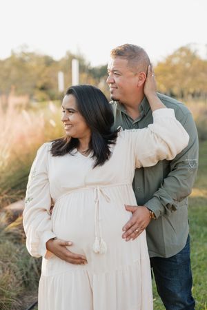 A couple embraces outdoors in a field during golden hour while wearing white and gray casual attire.