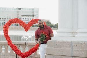 A couple poses together in front of a heart-shaped balloon display during a romantic outdoor photo session.