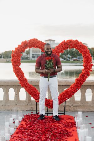 Large heart-shaped red rose petal arrangements on white balcony overlooking waterfront during romantic proposal setup.