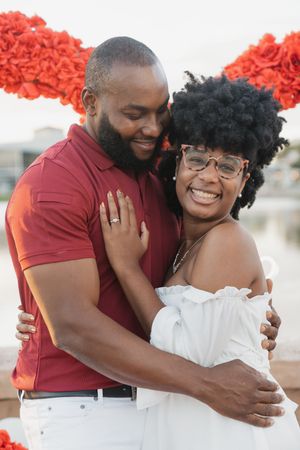 A couple shares joyful embraces and laughter in a series of romantic outdoor photos with red floral decorations.