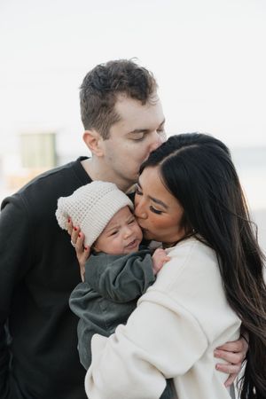 A family shares intimate cuddles and kisses during a beachside portrait session.