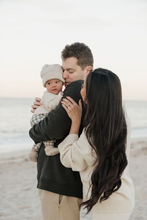 Family shares tender moments together on a peaceful beach at sunset wearing neutral colored clothing.