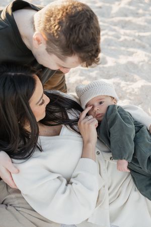 Family lying together on sandy beach sharing sweet moments and cuddles.