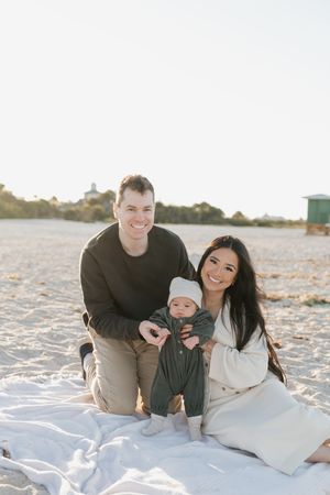 A family relaxes together on white sand during a beach photoshoot.