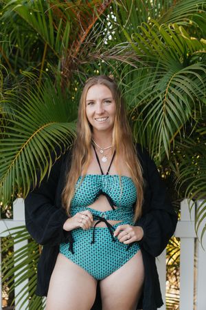 Person in a polka dot swimsuit and black cover up poses by tropical palm trees in an outdoor setting.
