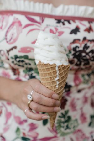 A series of hands holding waffle cones with vanilla ice cream against a floral patterned background.