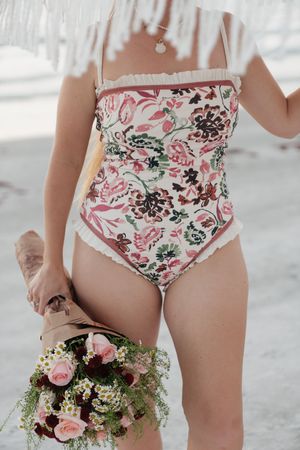 Person wearing floral swimwear holding a pink and white flower bouquet against a bright background.