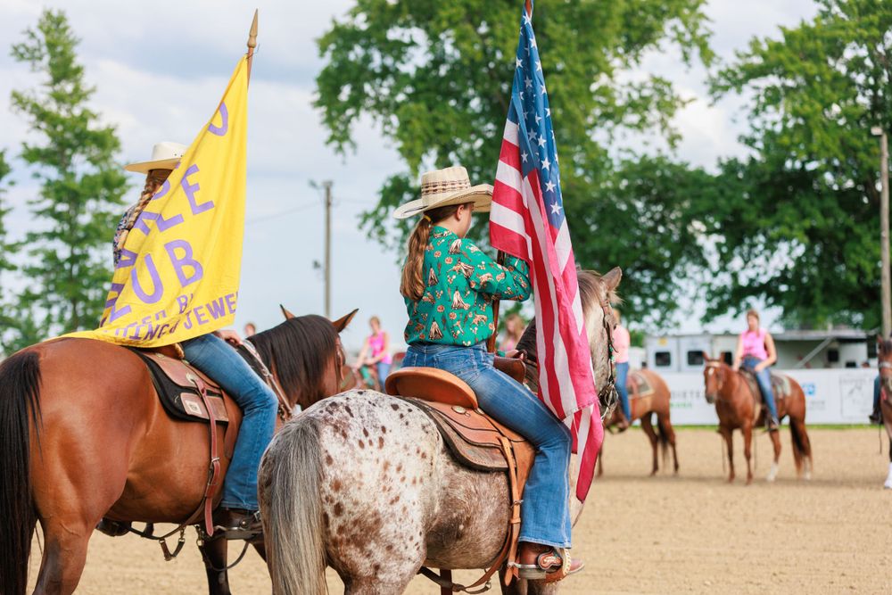 Horse club participants sit on their horses while proudly displaying the American flag and their club flag.