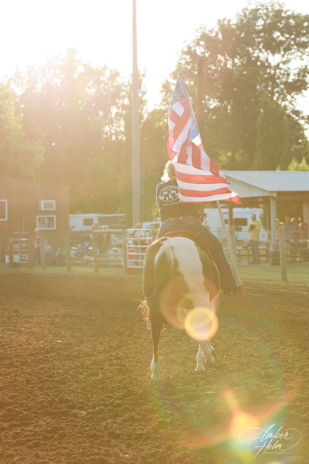 Sunset image of woman riding her paint horse and proudly carrying the American Flag at the Casey Saddle Club show.