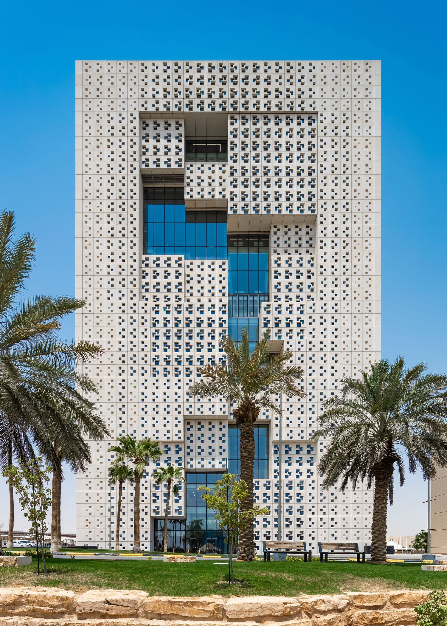 Modern office building with intricate geometric perforated facade and palm trees in the foreground against blue sky.