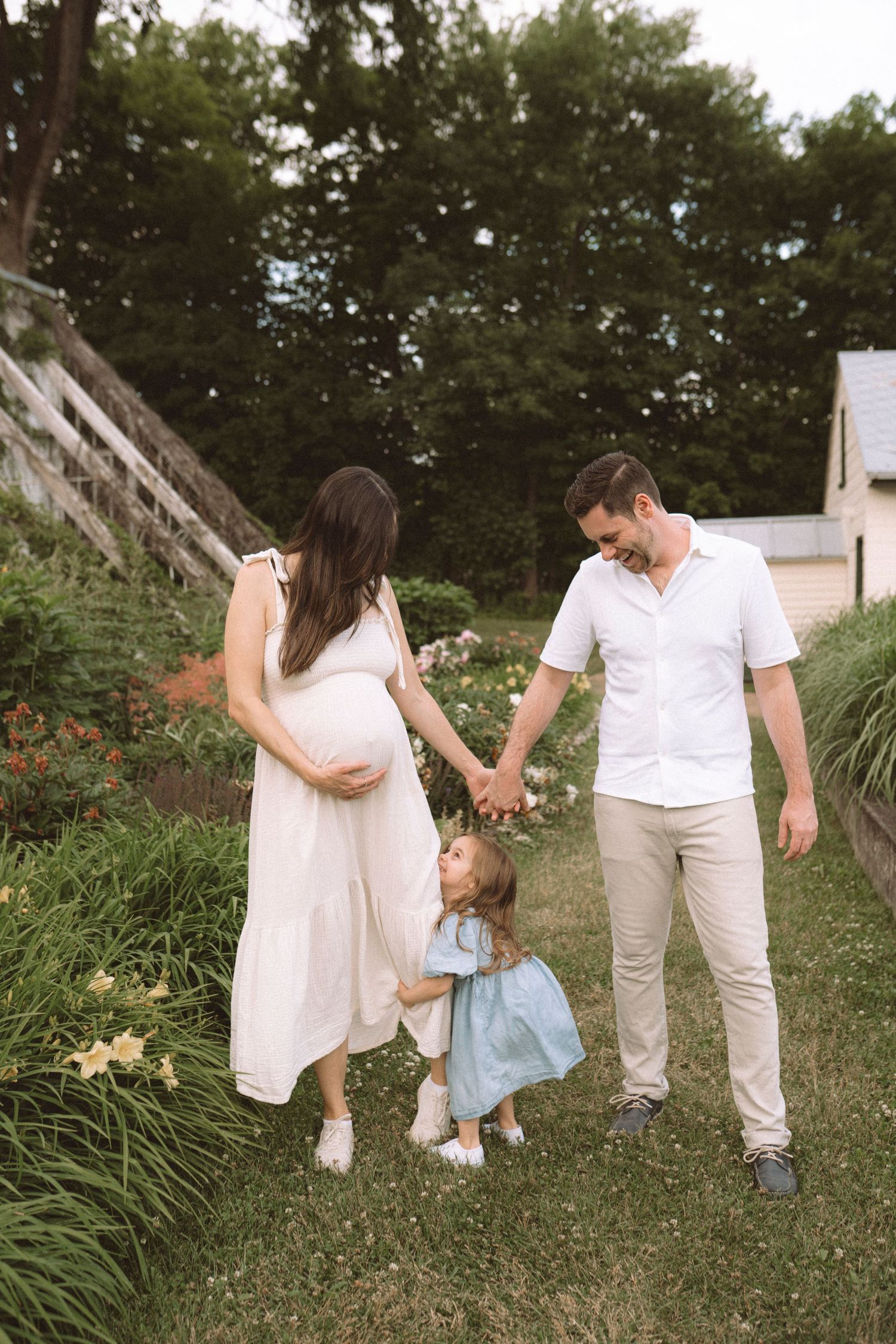 Family of three holding hands while walking together through garden pathway.