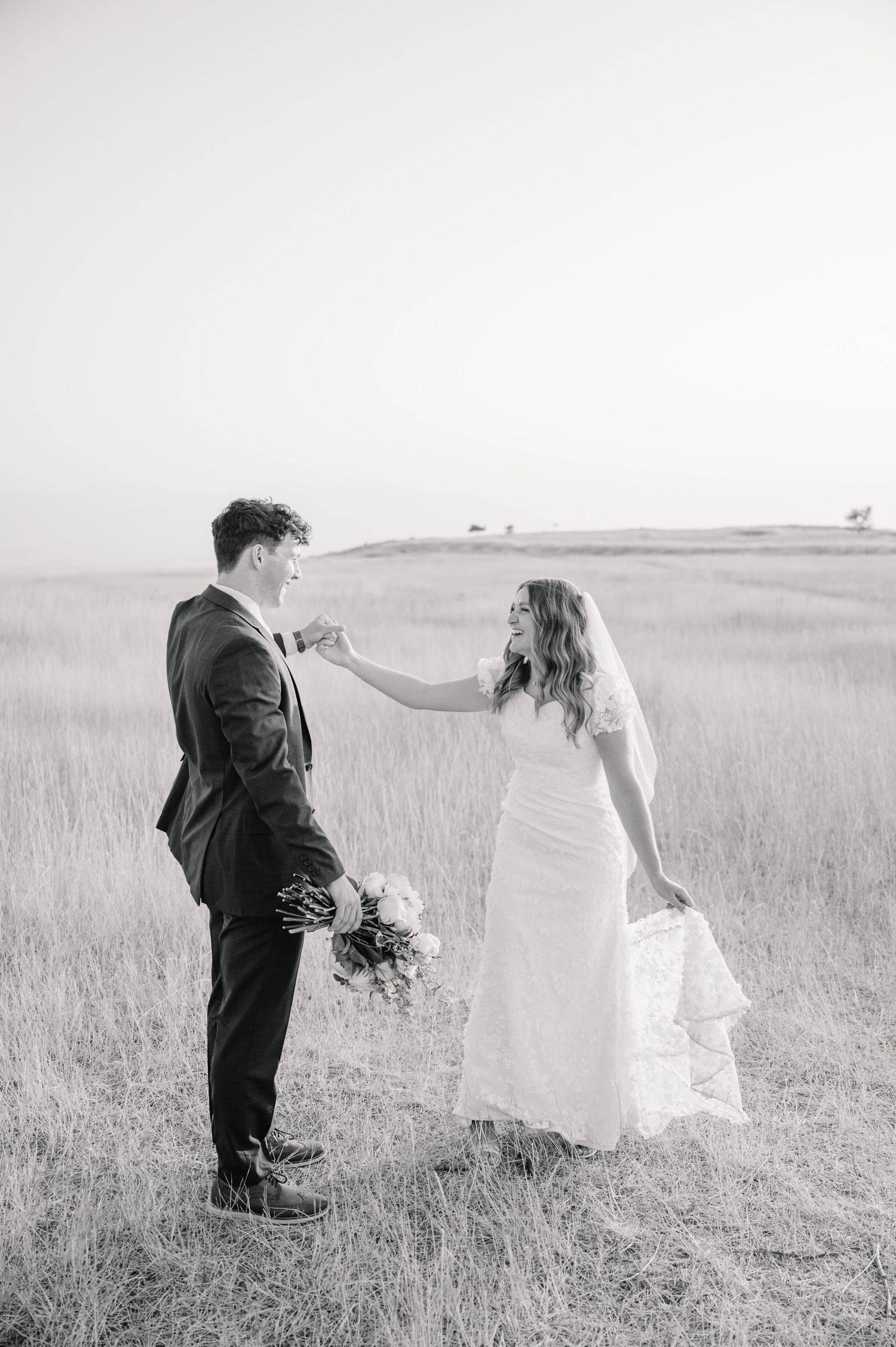 Black and white photo of couple sharing playful moment in field during wedding.