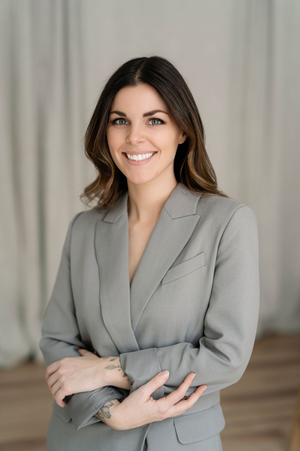 Professional headshot of woman in grey blazer with natural makeup and styled hair.