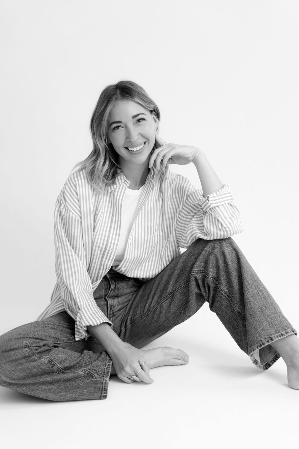 Black and white portrait of woman in striped shirt and jeans sitting casually.