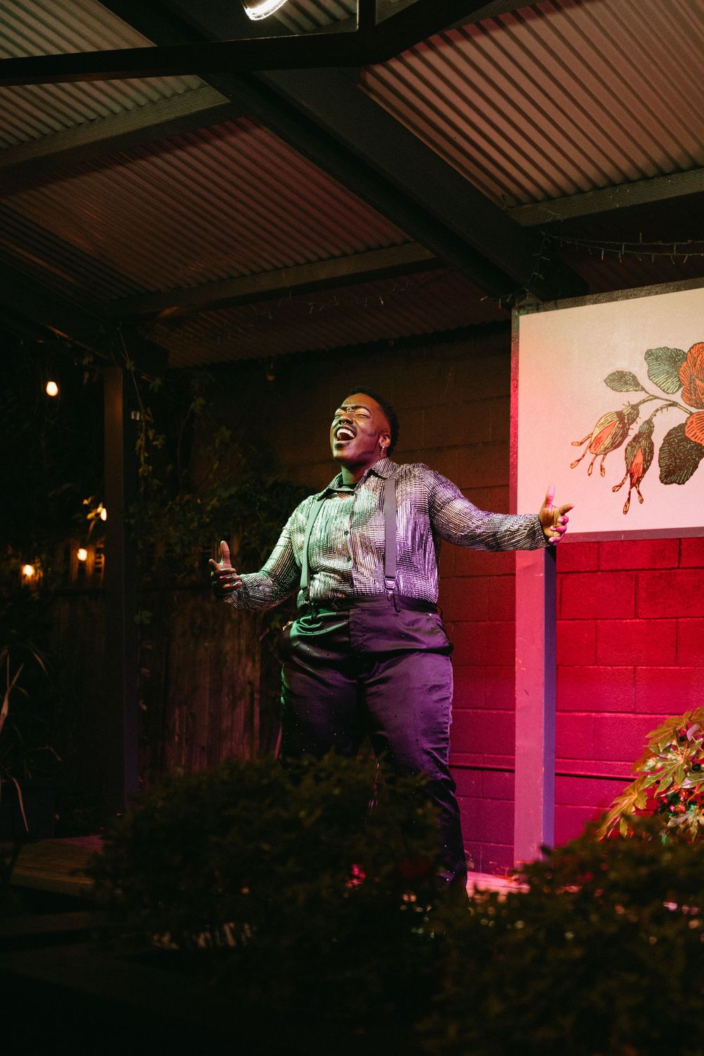 A performance artist moves expressively on stage under dramatic red and purple lighting against a dark backdrop.