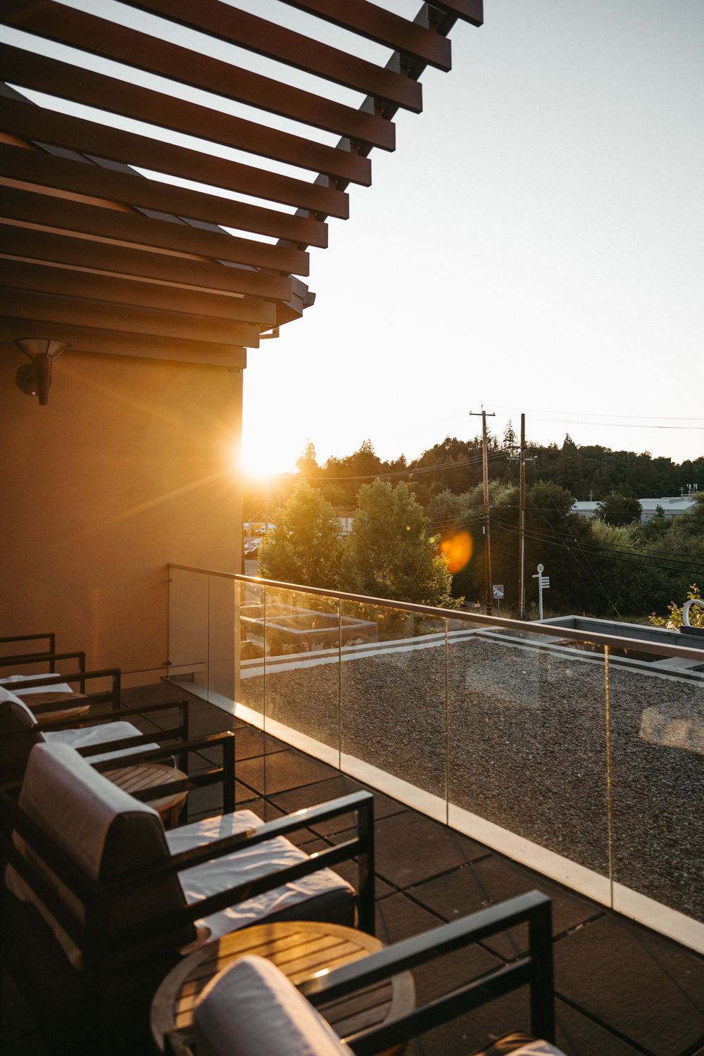 Modern patio with wooden pergola and glass railing captures golden sunset views over urban rooftops.