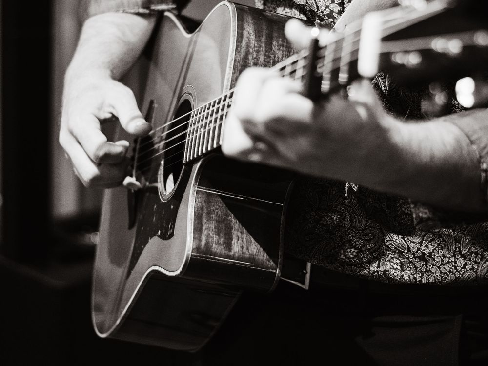Black and white close-up photo of hands strumming an acoustic guitar during a performance.