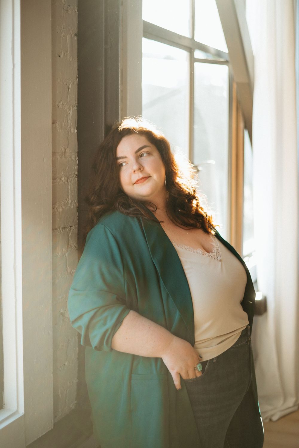 Dreamy sunlit portrait of someone in a teal cardigan leaning against a window with warm golden light streaming in.