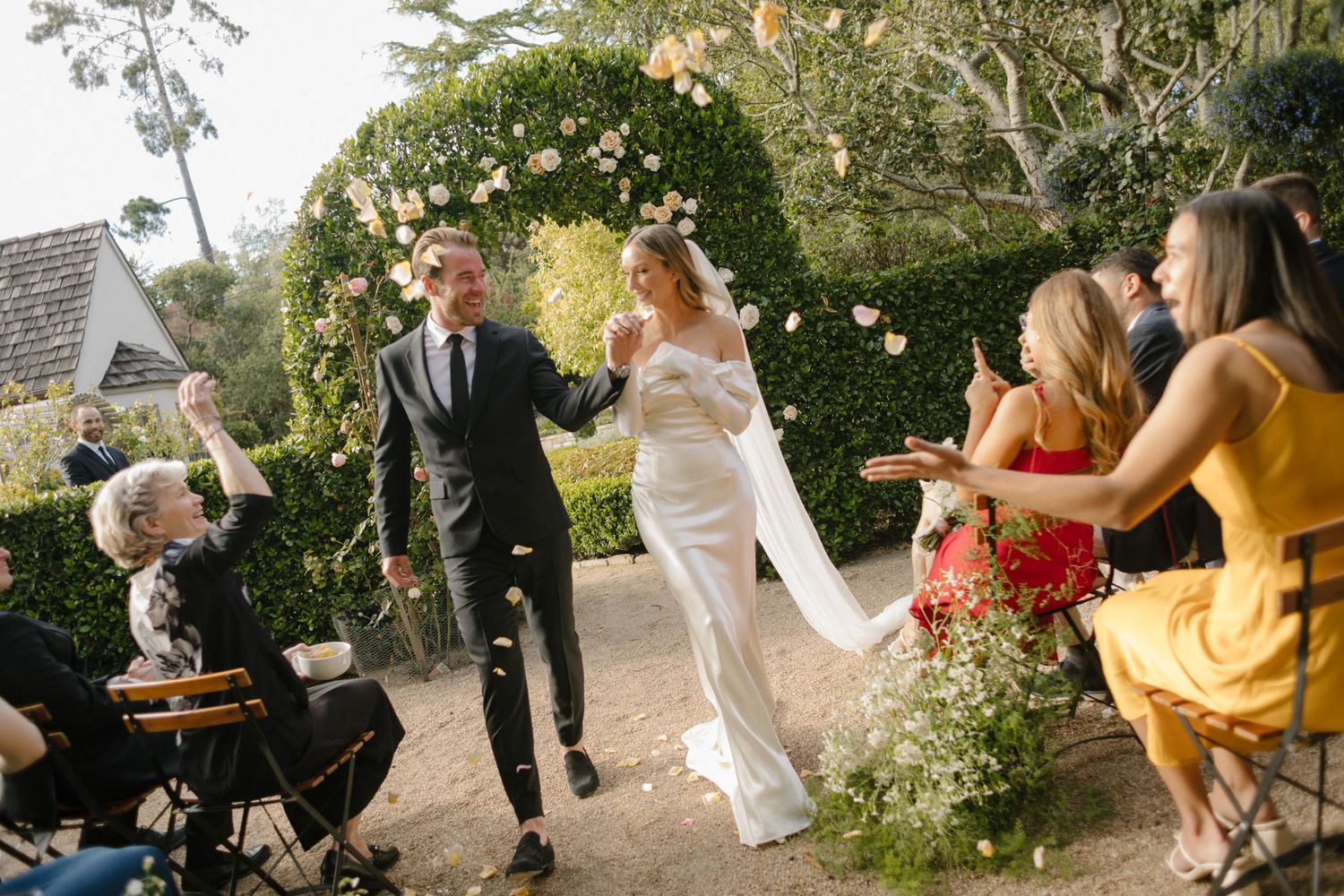 Wedding celebration with guests dancing outdoors under garden arch.