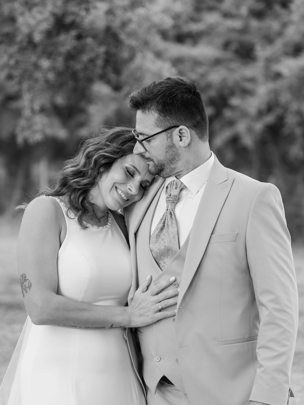 A tender romantic black and white portrait of a newlywed couple embracing outdoors in elegant wedding attire.