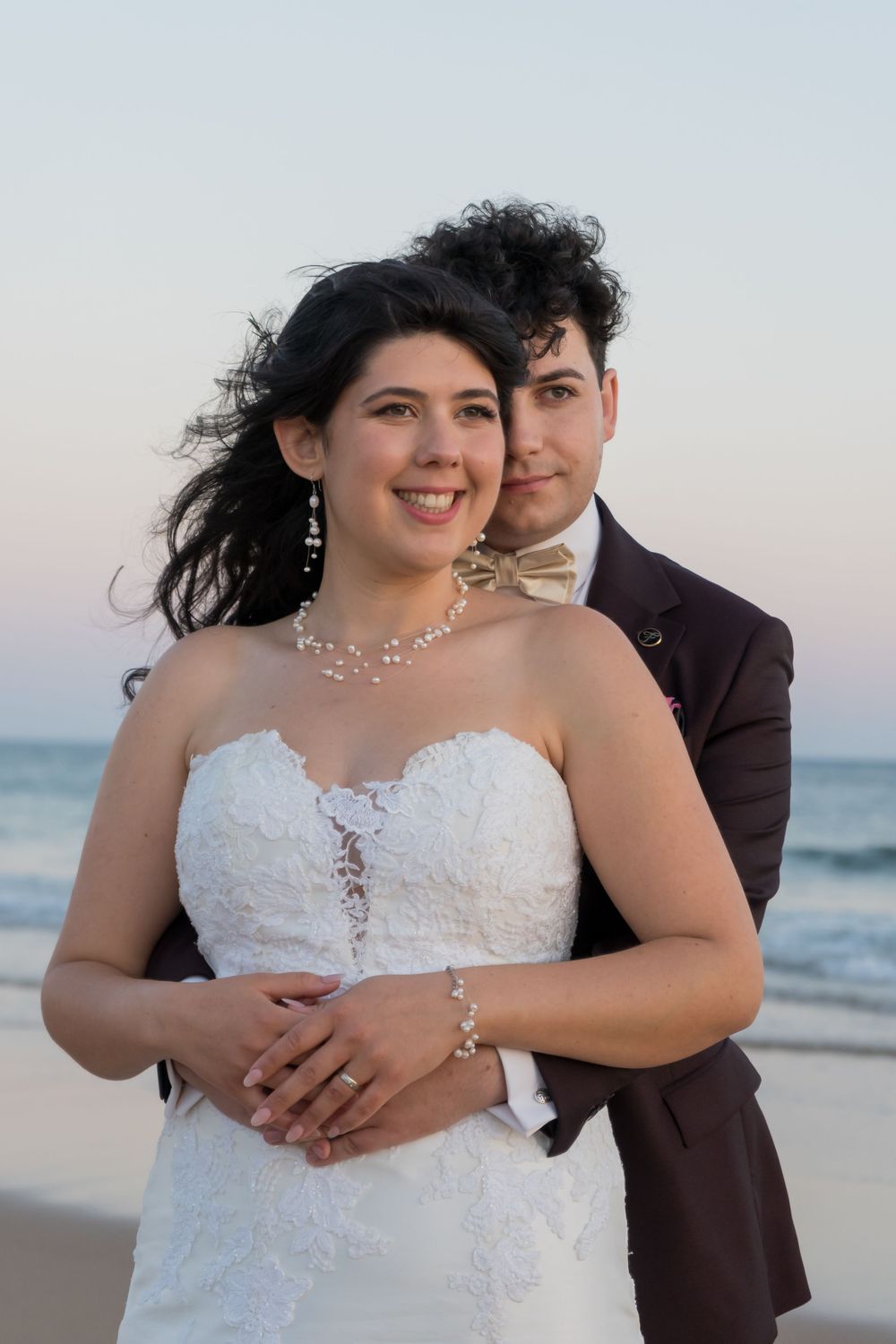 A romantic beach wedding portrait with a couple embracing, with the ocean in the background at sunset.