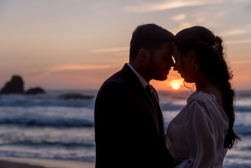 A romantic silhouette of a couple touching foreheads on the beach at sunset with ocean waves in the background.